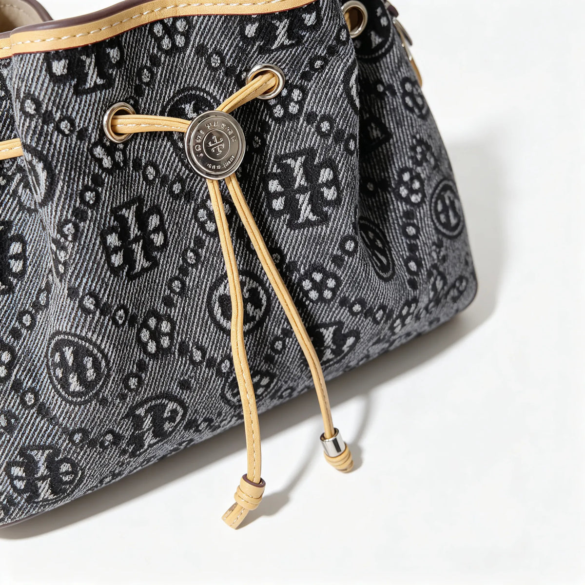 Tory Burch | Dark washed denim bucket bag with side pockets and drawstring closure featuring a T-print pattern
