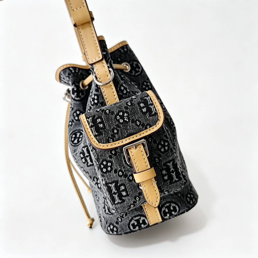 Tory Burch | Dark washed denim bucket bag with side pockets and drawstring closure featuring a T-print pattern