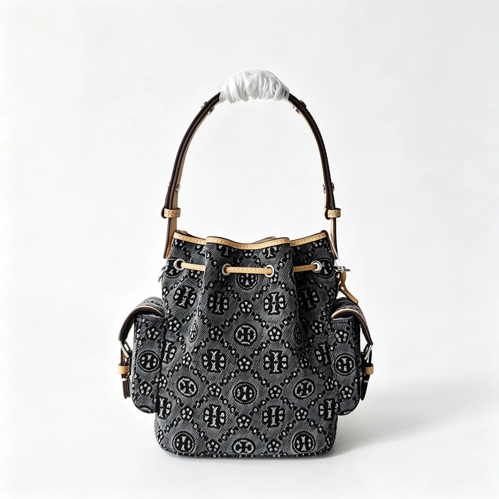 Tory Burch | Dark washed denim bucket bag with side pockets and drawstring closure featuring a T-print pattern